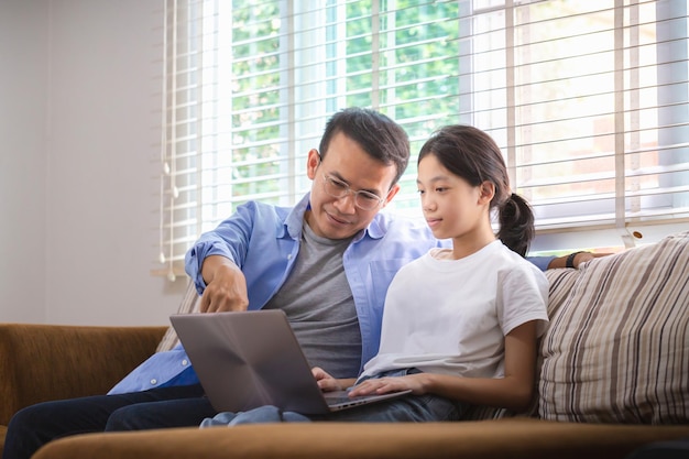 Asian father and daughter using laptop at home People doing activities and family concepts