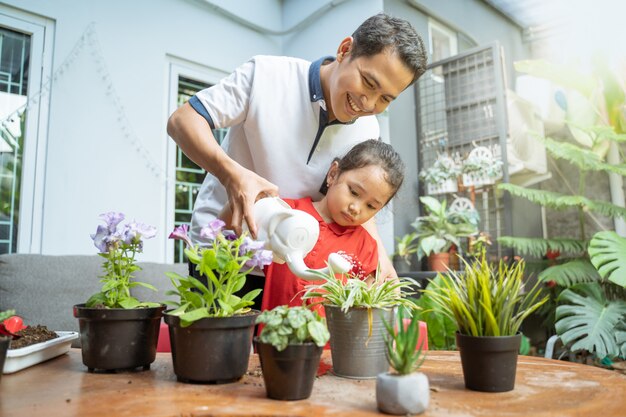 鉢植えの植物に水をまくために水まき缶を使用してアジアの父と娘