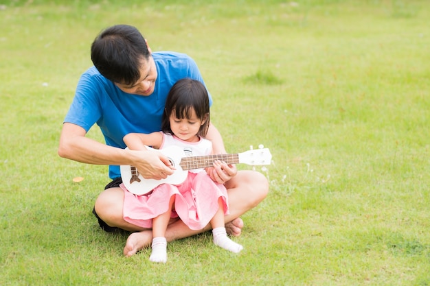 Il padre asiatico sta insegnando a sua figlia a suonare l'ukulele con un momento di felicità totale