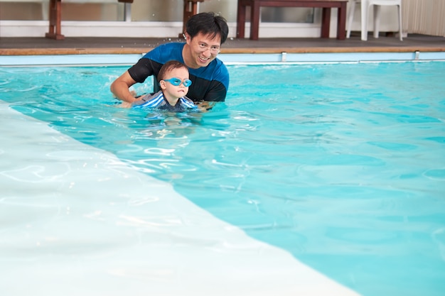 Asian Father and son takes a swimming lesson at indoor swimming pool, Cute little Asian 2 years old toddler boy child wearing swimming goggles learning to swim