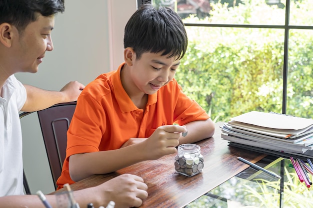 Asian father and son teaching son to Financial Literacy save money Dad and children putting money to the money box fatherhood