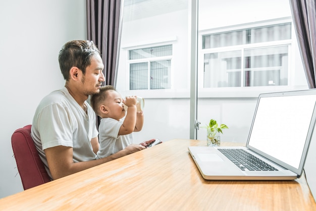 Asian father and son using smart phone and laptop together in home background