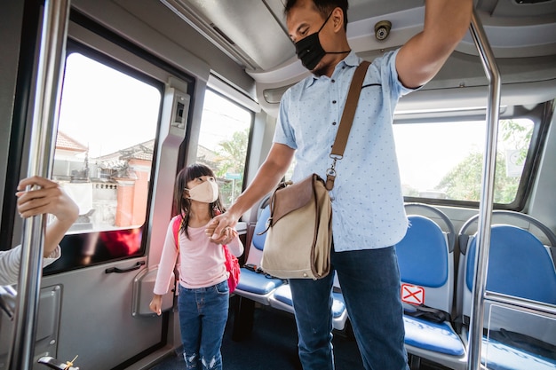 Asian father taking his daughter to school by riding bus public transport wearing a face mask