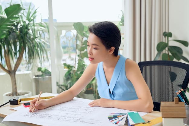 Asian female architect studying plans in office