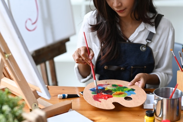 Foto artista femminile asiatico che mescola colore sulla tavolozza alla sua officina.