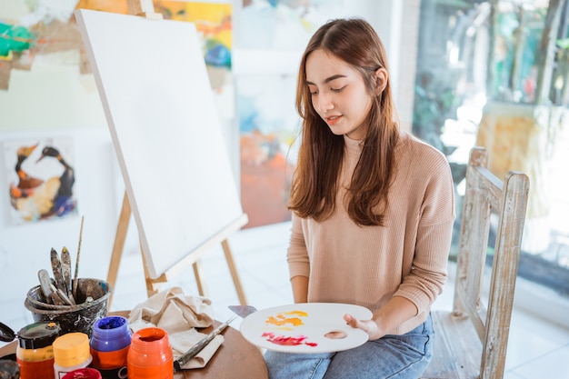 Asian female artist painting on canvas doing some art projects on her studio workshop