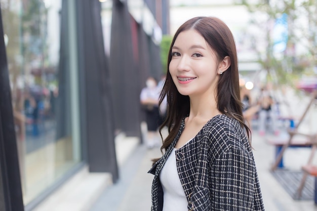 Asian female in a black pattern coat with braces on teeth walking and smiling outdoors in the city