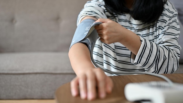 An Asian female checking her blood pressure with blood pressure monitor by herself cropped