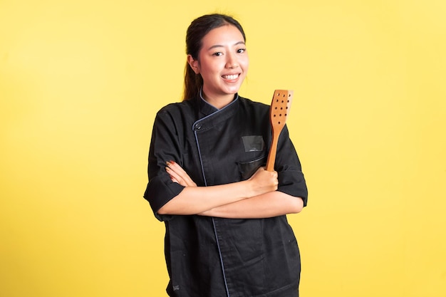 Asian female chef smiling with hands crossed and holding spatula on isolated background