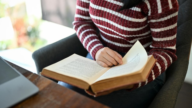 Asian female college student reading a book while sitting in the campus library cropped image