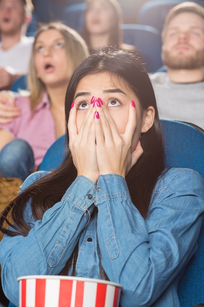 asian female covering her mouth with her hands terrified watching a movie at the cinema