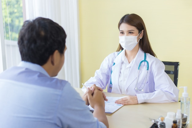 Asian female doctor
 Asking patient questions
 By wearing a surgical mask at all times