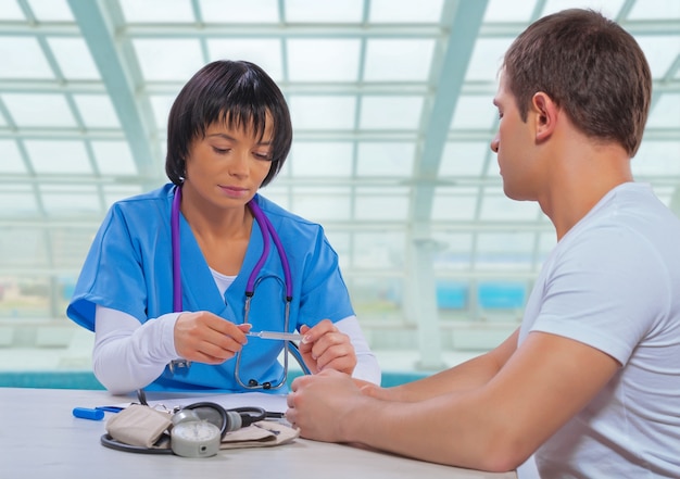 Medico femminile asiatico che osserva sul termometro medico e che si siede al tavolo con il paziente