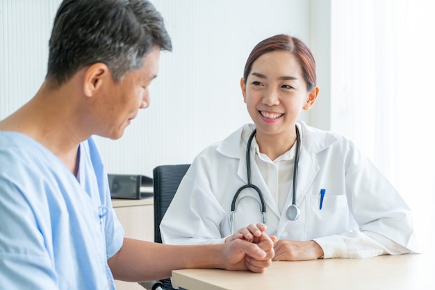 Азиатский женский доктор и пациент обсуждая что-то сидя за столом