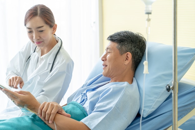 Азиатский женский доктор сидя на больничной койке и обсуждая с старшим пациентом