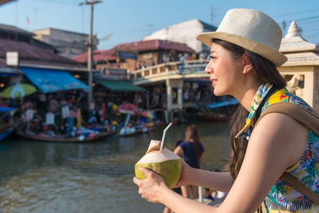 Asian female drinks the coconut drink and enjoy the pleasant view of the floating market.