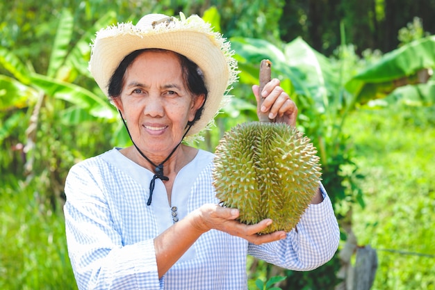 Asiatiche contadine anziane che indossano cappelli, con in mano 1 frutto di durian