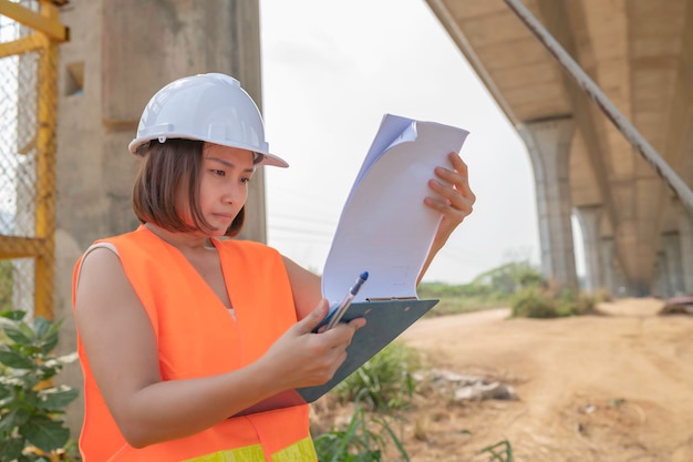 An asian female engineer works at a motorway bridge\
construction sitecivil worker inspecting work on crossing\
construction