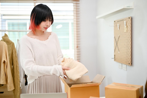 An Asian female fashion clothing seller packing a shipping product into a cardboard box