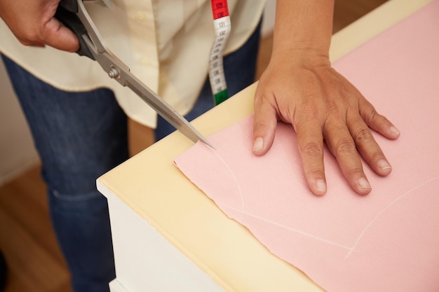 Asian female fashion designer cutting material at a studio workbench