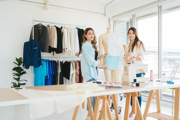 Asian female fashion designer or tailor with assistance pinning paper fabric pattern to mannequin Dressmaker working and designing new fashion collections for customers in an atelier tailor workshop