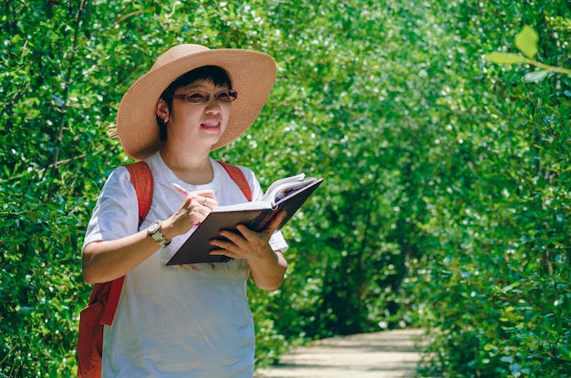 Asian female forester taking notes on walkway in mangrove forest at natural parkland