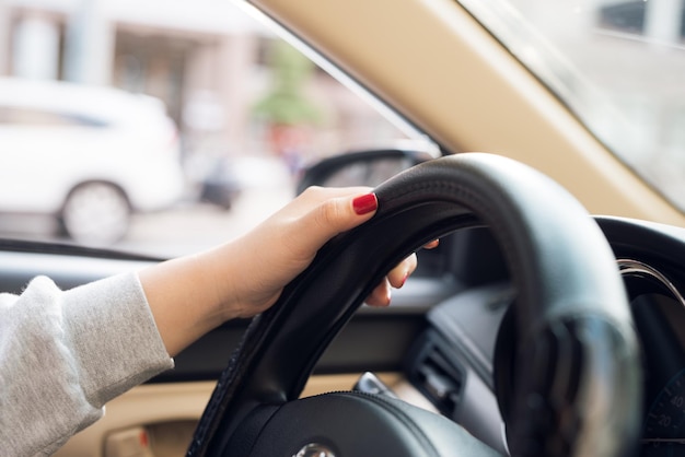 フロントガラスと道路で運転している間、アジアの女性が車のハンドルを握ります。自信を持ってハンドルを握っている黒人女性の手。ハンズオンホイール-車を運転する女性-アジア