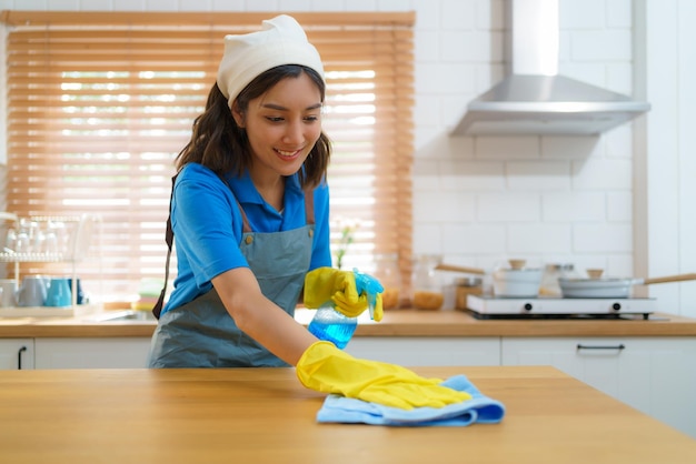 Asian female housewife using table cloth and sprayer in kitchen at homexA