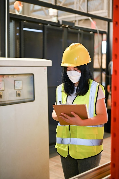 Asian female industrial engineer or worker checking list on her\
clipboard working in factory