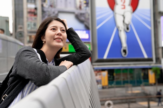 asian female leaning on the bridge in Dontonbori. looking at somewhere else.