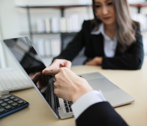 Asian female manager pointing at laptop screen for colleague while working on business project in modern office. Team and training concept.