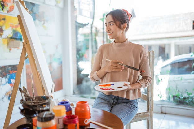 Asian female painter painting on canvas in her workshop