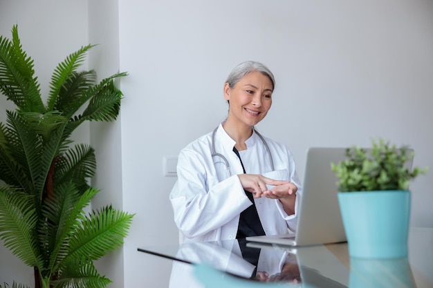 Asian female physician communicating in sign language with patient by video