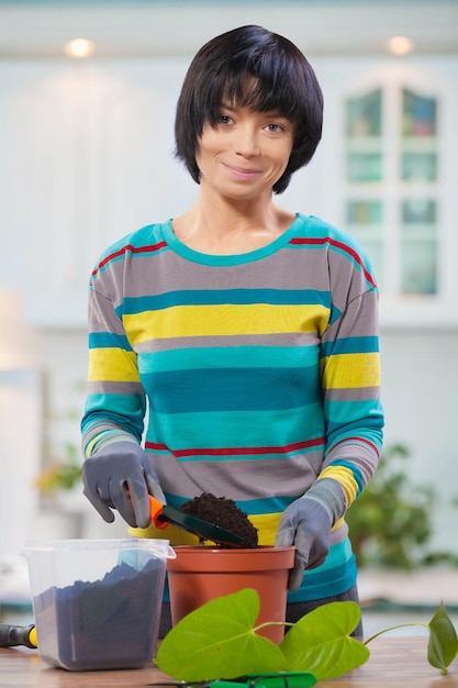 Asian female pouring ground in pot for repotting flower