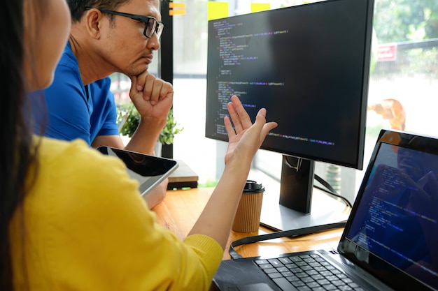 Asian female programmers wearing yellow shirts are pointing at their laptop screen for presentation to executives.