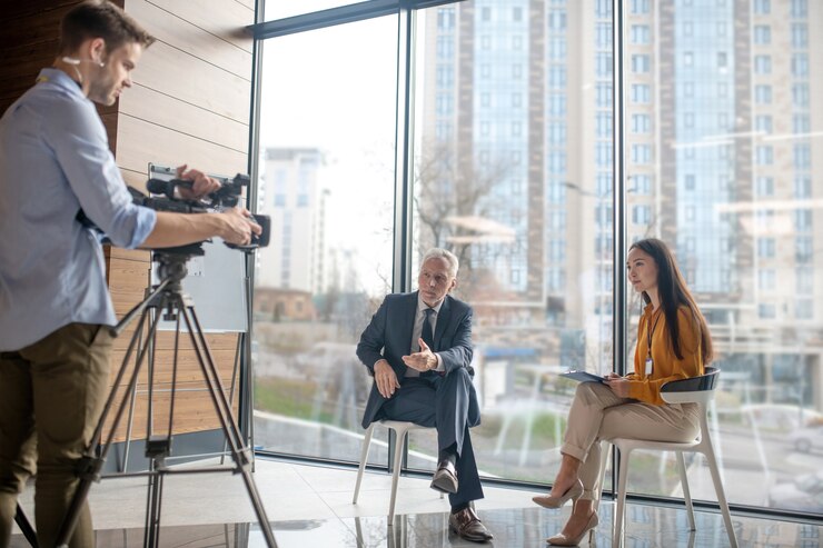 Asian female reporter siting in the studio talking to a gray-haired man