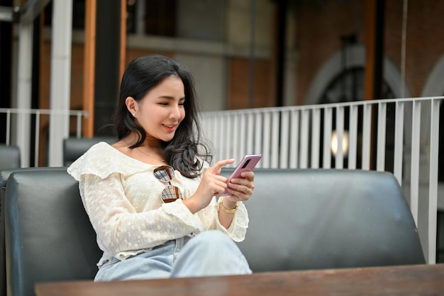 그녀의 친구와 채팅 그녀의 스마트 폰을 사용하여 야외 공간에 카페에서 쉬고 아시아 여성