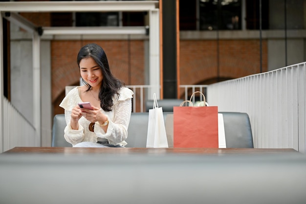 Asian female resting at the shopping mall relaxation area using her smartphone