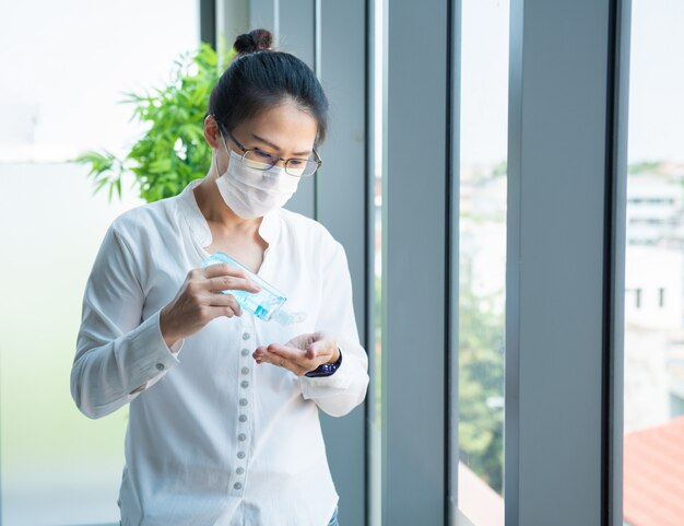 Азиатское женское серьезное мышление и носить маски в модельном офисе смотрят в окно