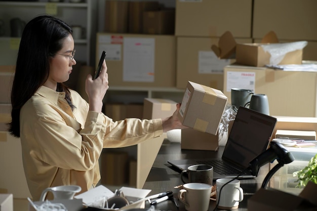 스마트폰에서 모바일 앱을 사용하여 소포 상자를 확인하는 아시아 여성 소기업 소유자