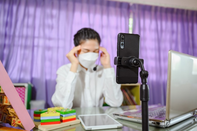 Insegnante asiatica che pensa intensamente e stressata seduta triste indossa una maschera mentre studia online. video online per l'istruzione