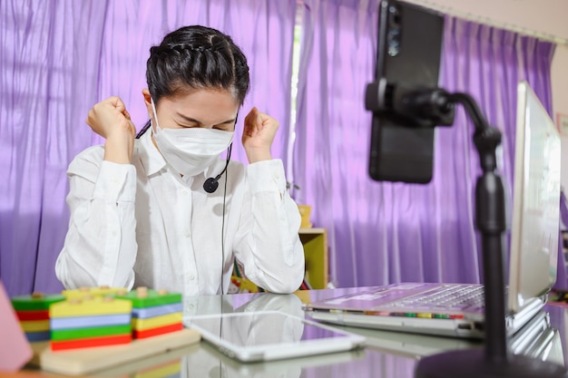 Asian female teacher thinking hard and stressed sitting sad She wears a mask while studying online. online video for education