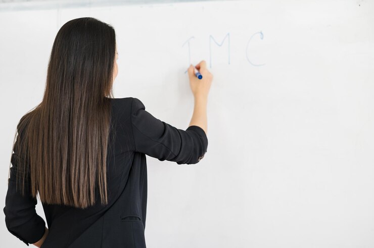 An Asian female teacher wearing black stands in front of a whiteboard in front of a classroom at university. Education concept, graduation, university teacher caree