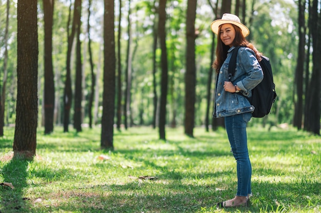 Una donna asiatica che viaggia con un cappello e uno zaino guardando in una bellissima pineta