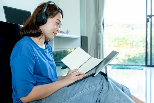 Азиатский женский студент университета носить наушники и смотреть ноутбук