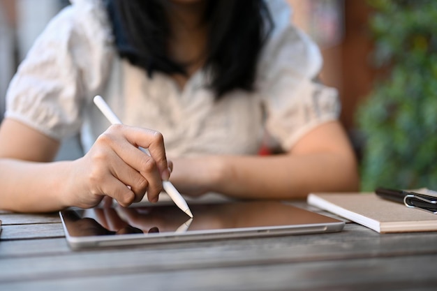 사진 야외 커피숍에서 휴식을 취하는 동안 태블릿에 스타일러스 펜을 사용하는 아시아 여성