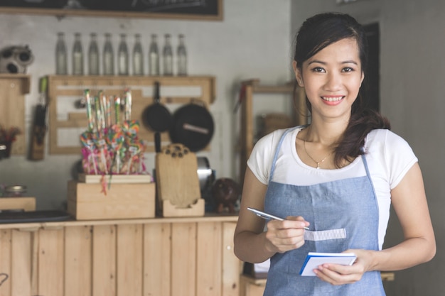 Asian female waiter in apron writing order