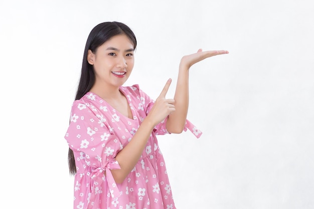 La femmina asiatica con i capelli lunghi neri in camicia rosa mostra qualcosa di presente su sfondo bianco