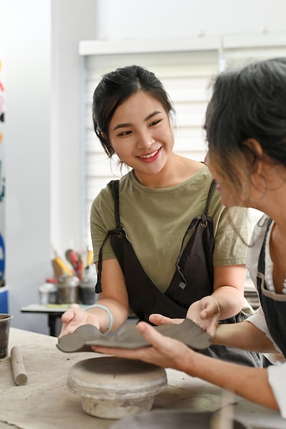 Insegnante di laboratorio femminile asiatica che aiuta una donna anziana a realizzare un piatto di argilla laboratorio di artigianato