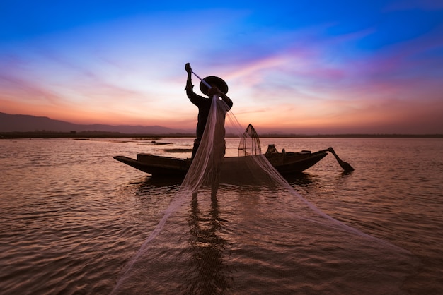 Pescatore asiatico con la sua barca di legno nel fiume della natura al mattino presto prima dell'alba